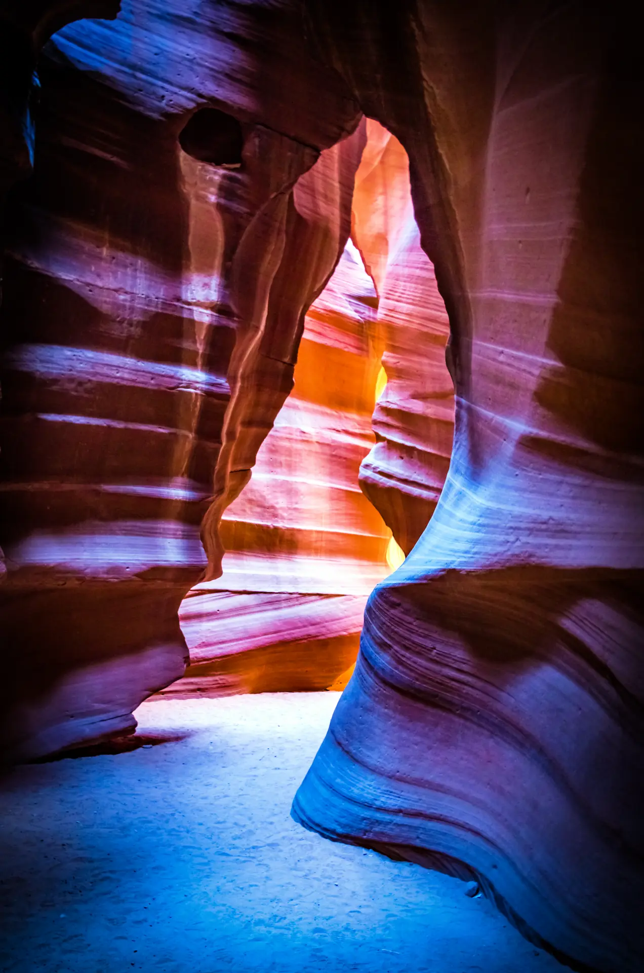 Antelope Canyon, Arizona, landscape photograph. Sunlight filters into a slot canyon, illuminating the sculpted, wavy sandstone walls in warm hues of orange, red, and purple.